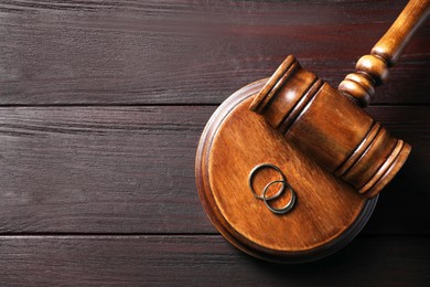 Divorce concept. Gavel and wedding rings on black wooden table, top view with space for text