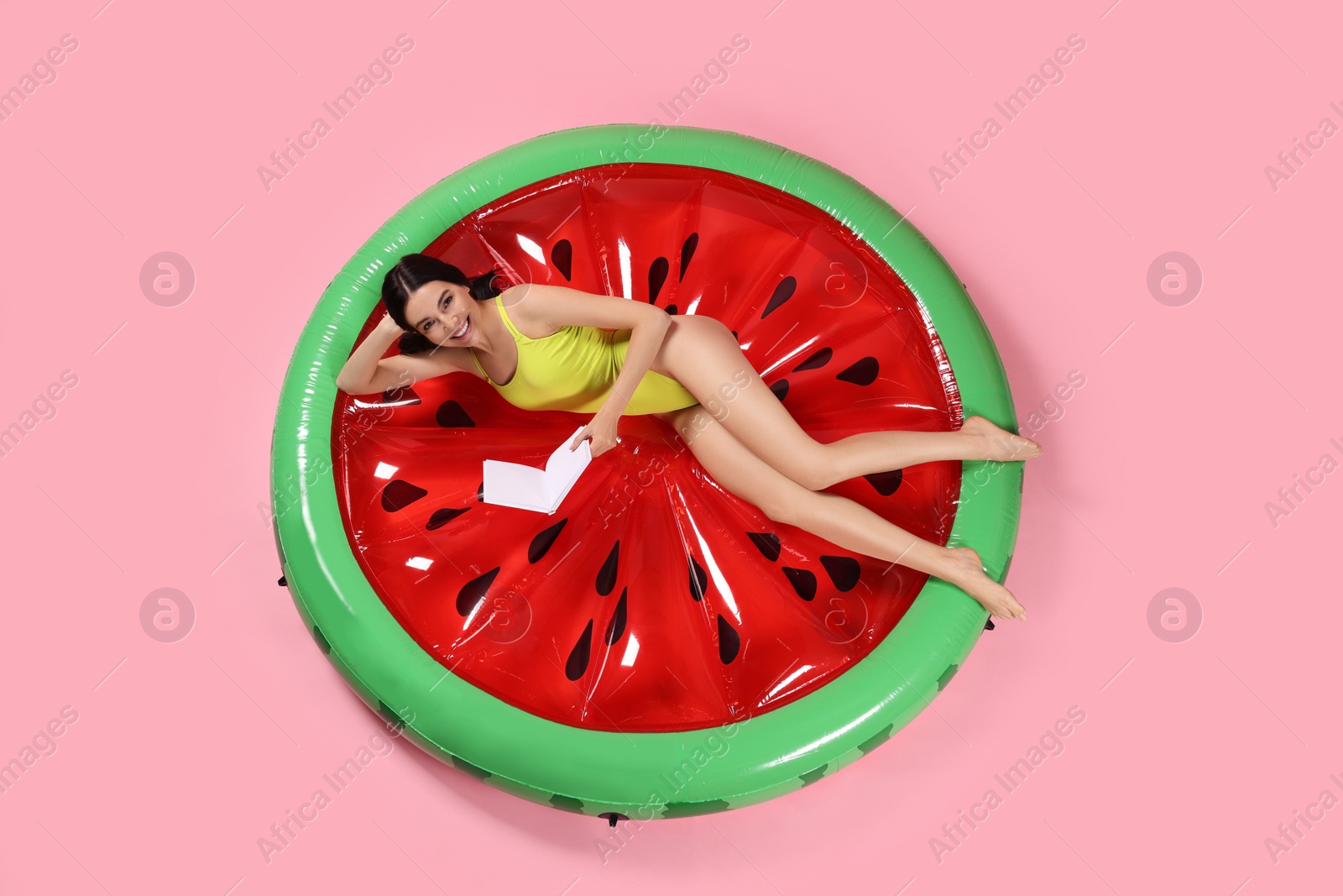 Photo of Young woman with book on inflatable mattress against pink background, above view