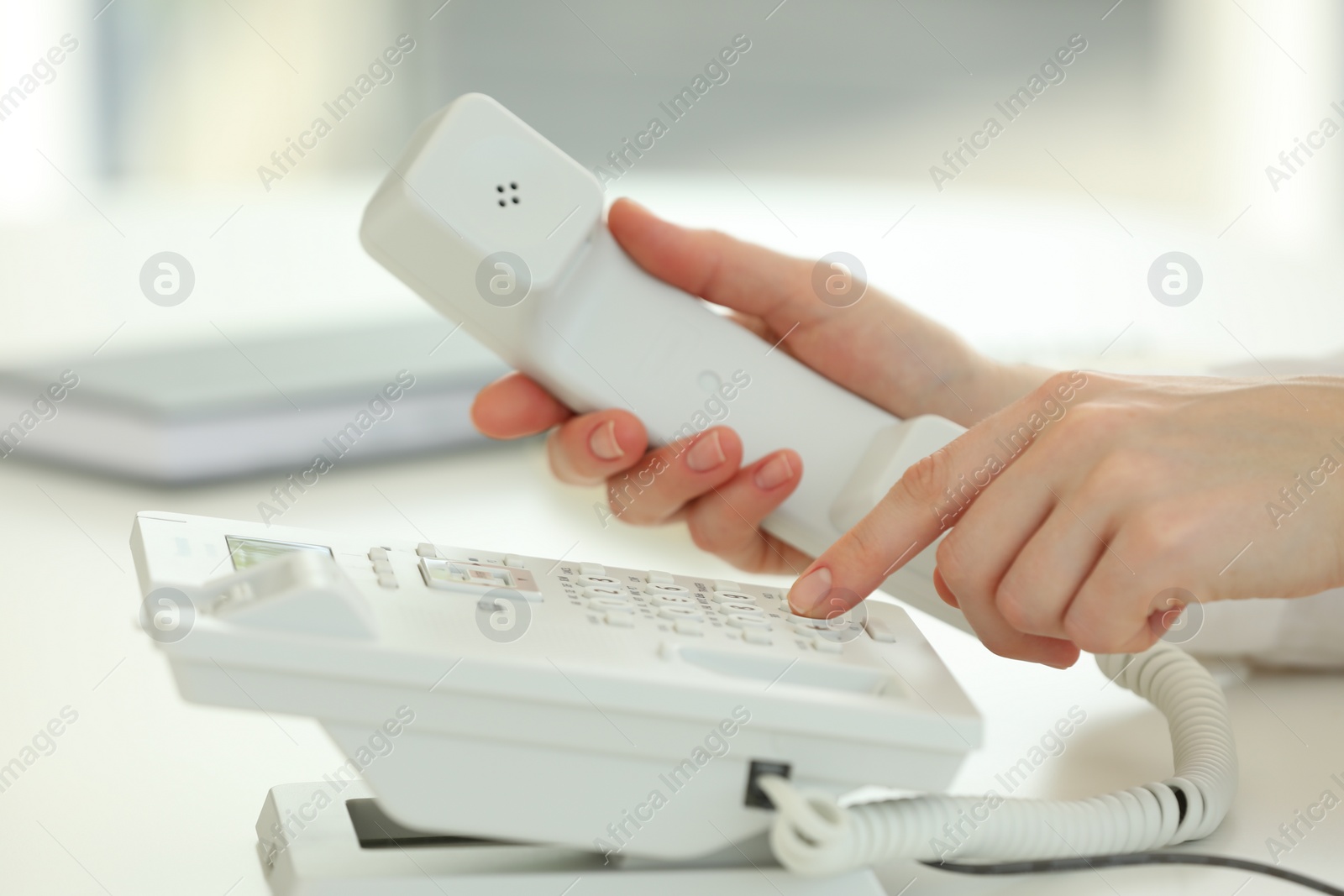 Photo of Assistant dialing number on telephone at white table, closeup