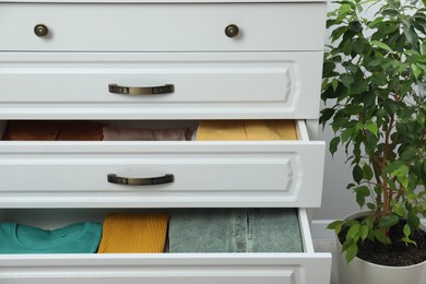 Photo of Sorting and organizing. Chest of drawers with different folded clothes indoors