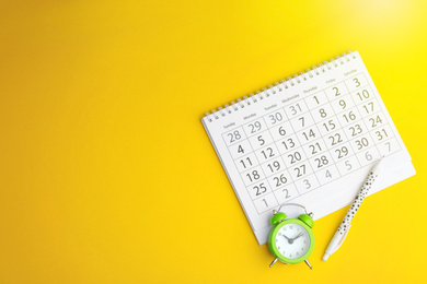 Calendar, pen and alarm clock on yellow background, flat lay. Space for text