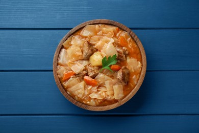 Tasty cabbage soup with meat, carrot and parsley on blue wooden table, top view