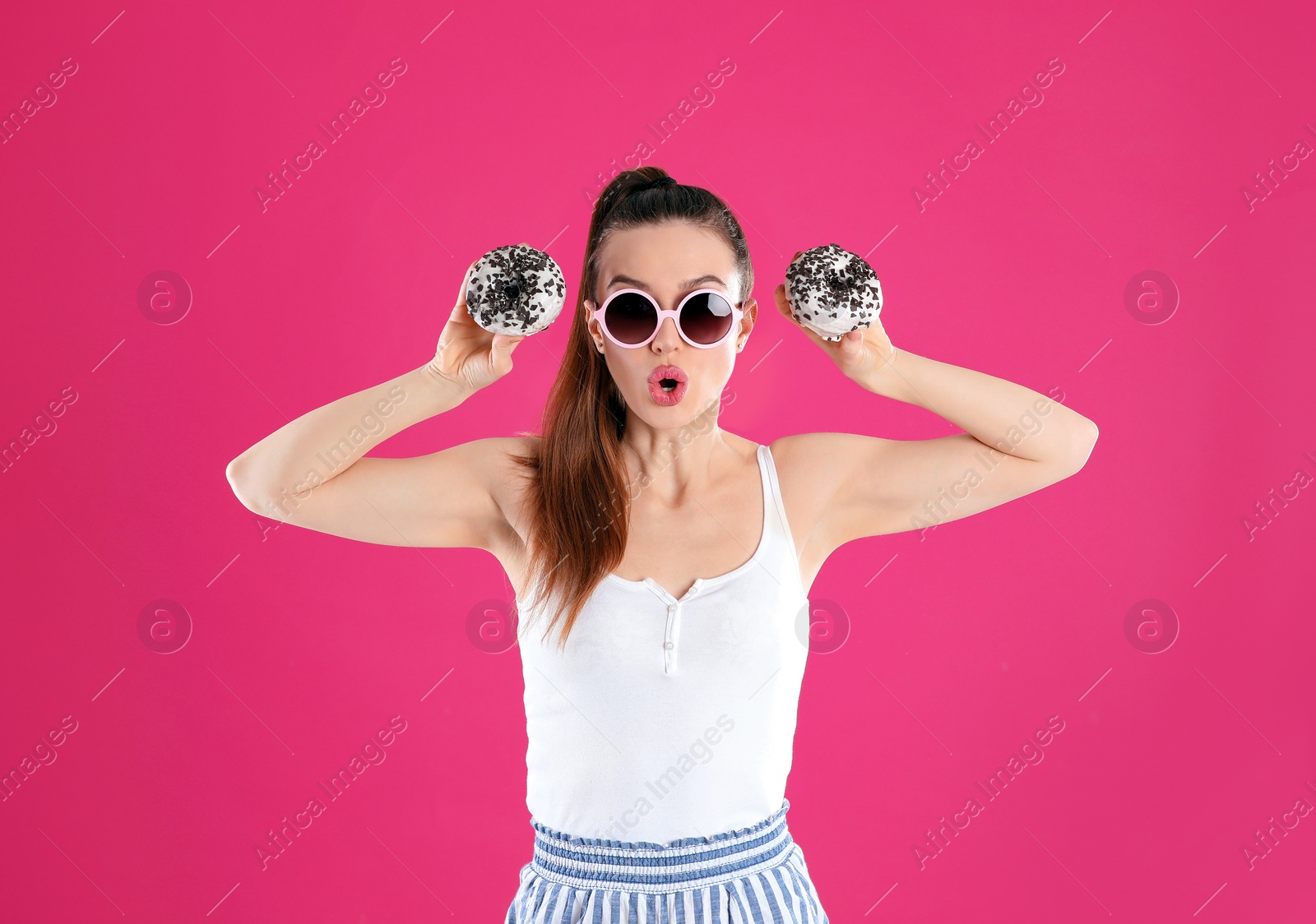 Photo of Beautiful young woman wearing sunglasses with donuts on pink background