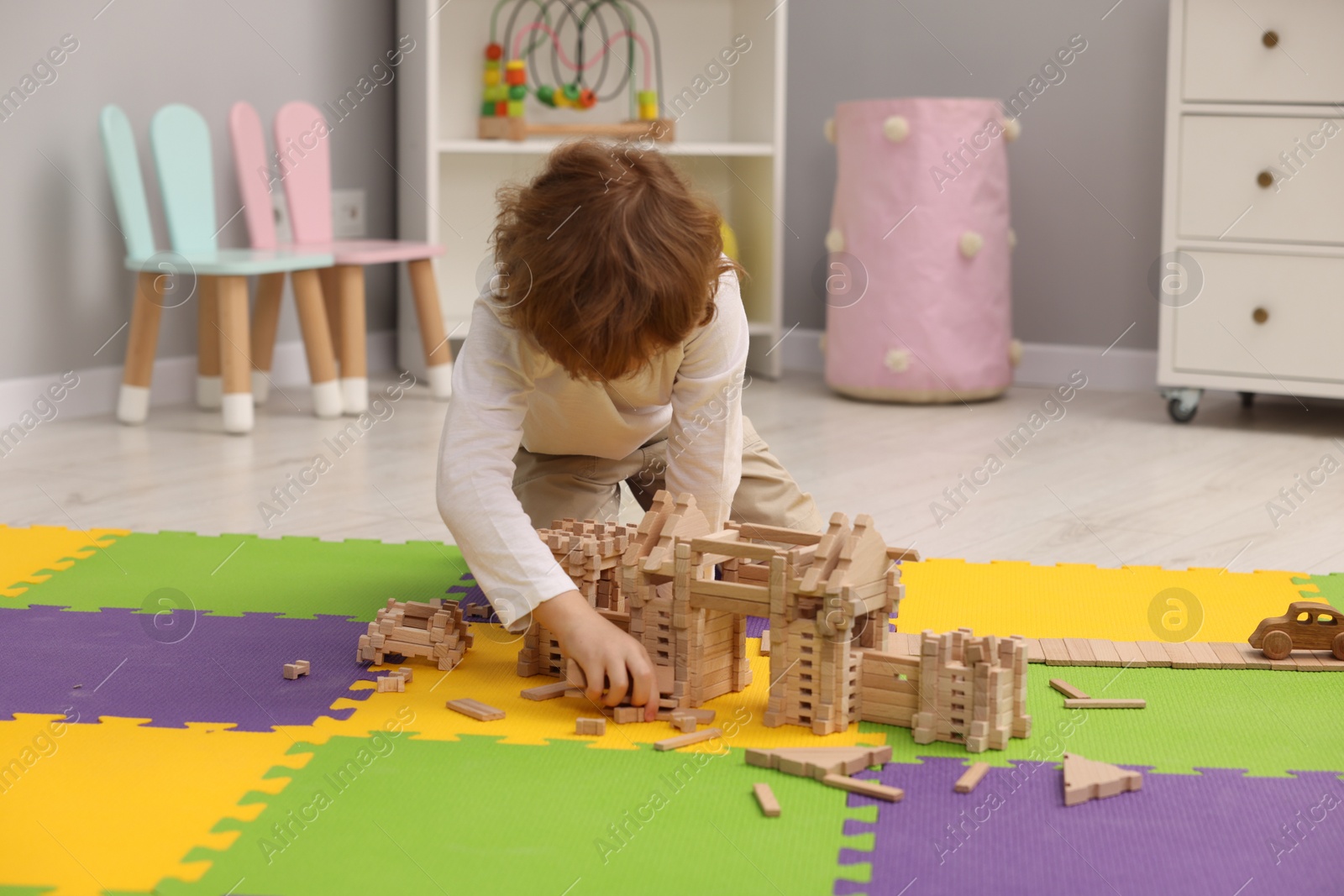 Photo of Little boy playing with wooden construction set on puzzle mat in room. Child's toy