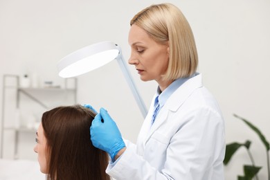 Photo of Trichologist examining patient`s hair under lamp in clinic