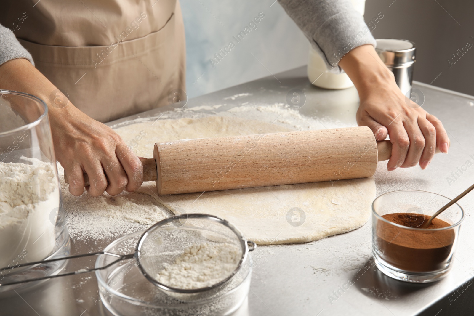 Photo of Woman rolling dough for cinnamon rolls on table, closeup