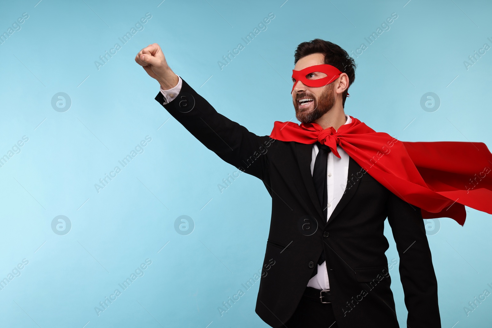 Photo of Businessman wearing red superhero cape and mask on light blue background