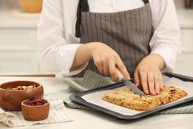 Photo of Woman cutting granola bars at table in kitchen, closeup