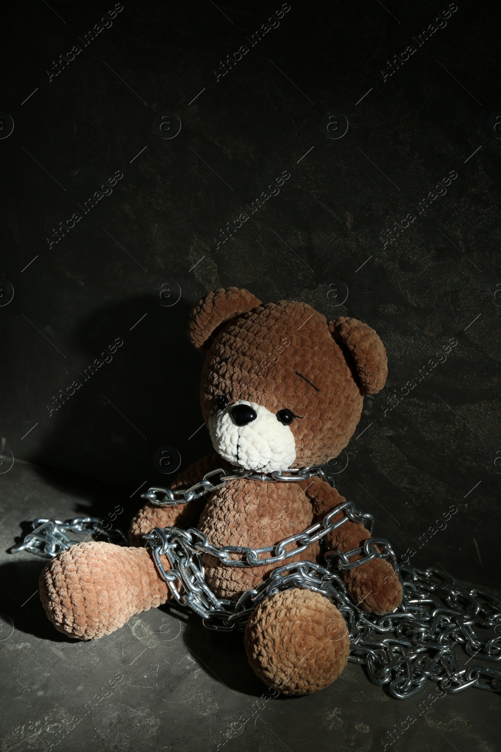 Photo of Stop child abuse. Chained toy bear in dark room