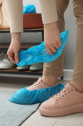 Photo of Woman wearing blue shoe covers onto her sneakers indoors, closeup