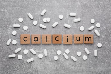 Photo of Word Calcium made of cubes with letters and pills on gray background, top view
