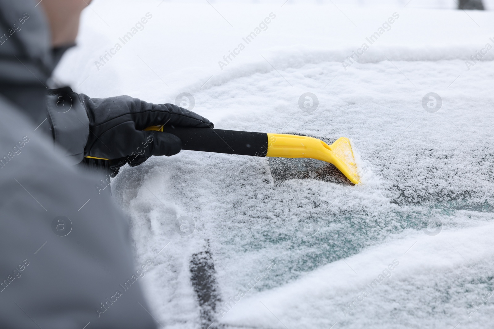 Photo of Man cleaning snow from car windshield outdoors, closeup