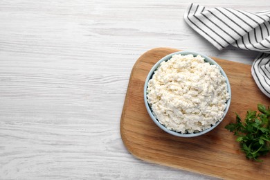 Delicious fresh cottage cheese with parsley on white wooden table, flat lay. Space for text