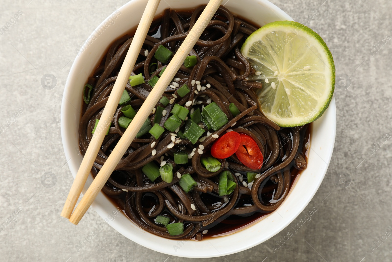 Photo of Tasty buckwheat noodles (soba) with sauce, onion in bowl and chopsticks on light grey table, top view