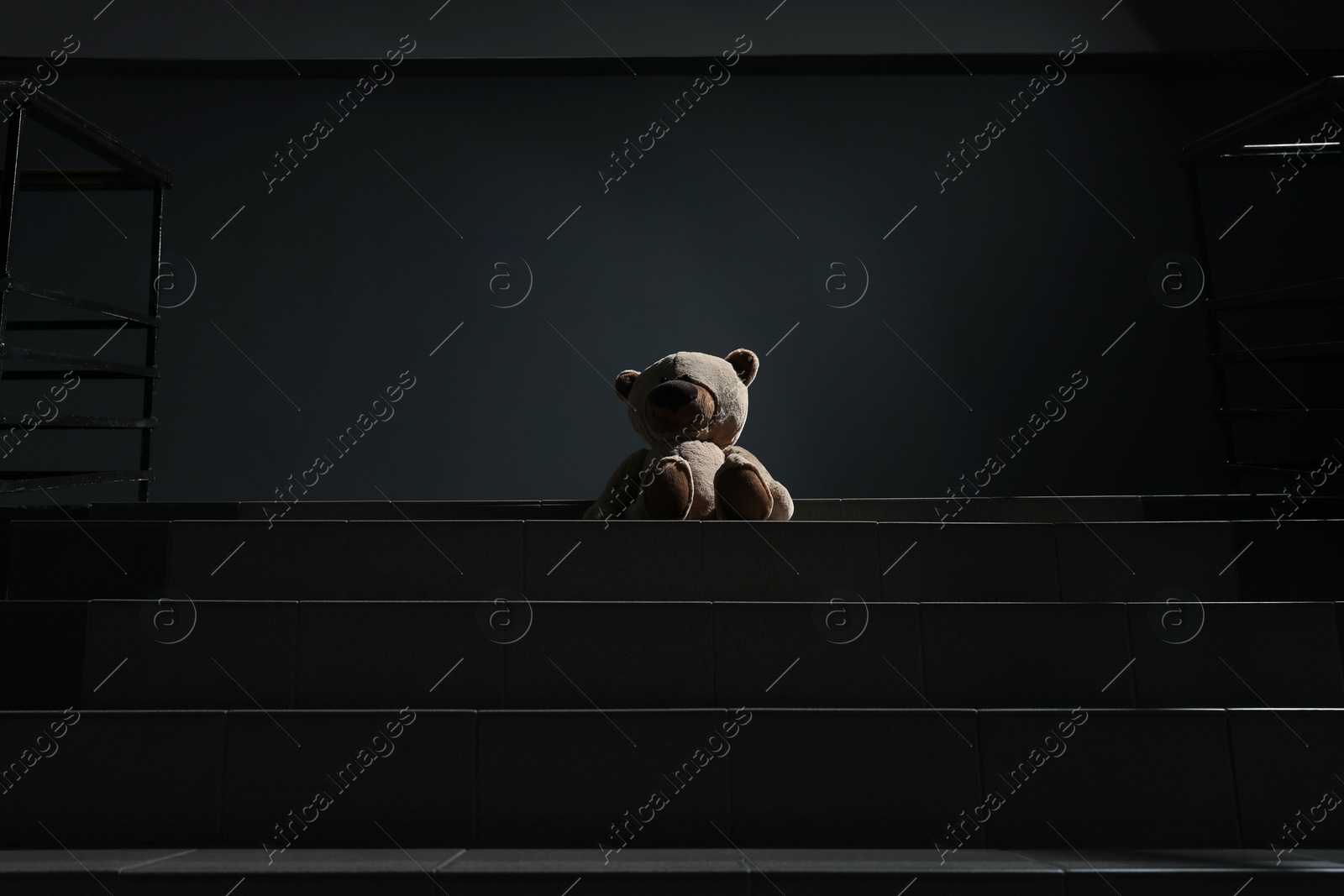 Photo of Lonely teddy bear on grey stairs indoors, low angle view