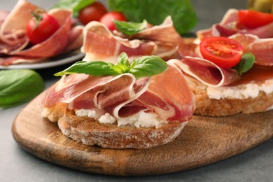 Photo of Board of tasty sandwiches with cured ham, basil, tomato and cream cheese on grey table, closeup