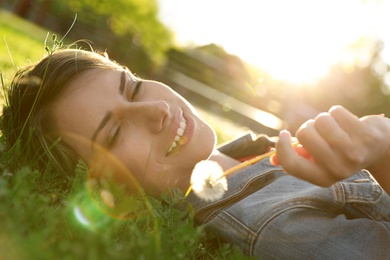 Young woman with dandelion in park on sunny day. Allergy free concept