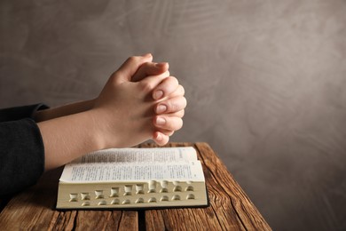 Woman praying over Bible at wooden table, closeup