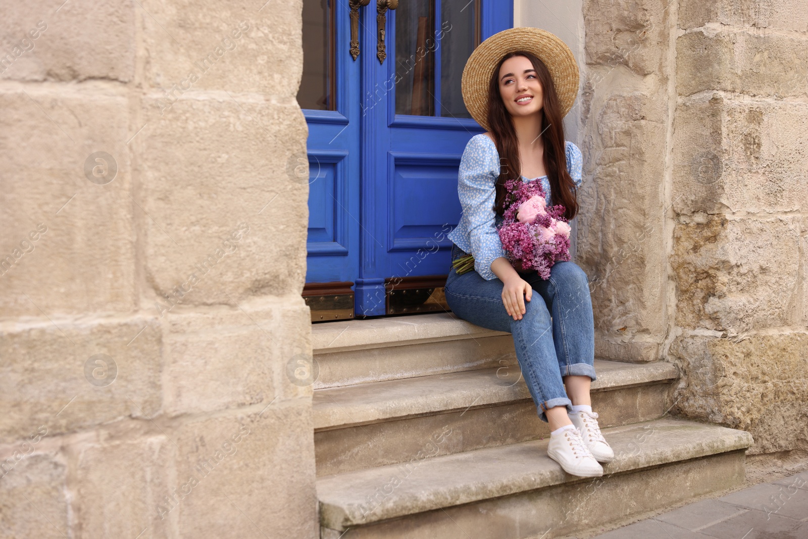 Photo of Beautiful woman with bouquet of spring flowers on stairs near building, space for text