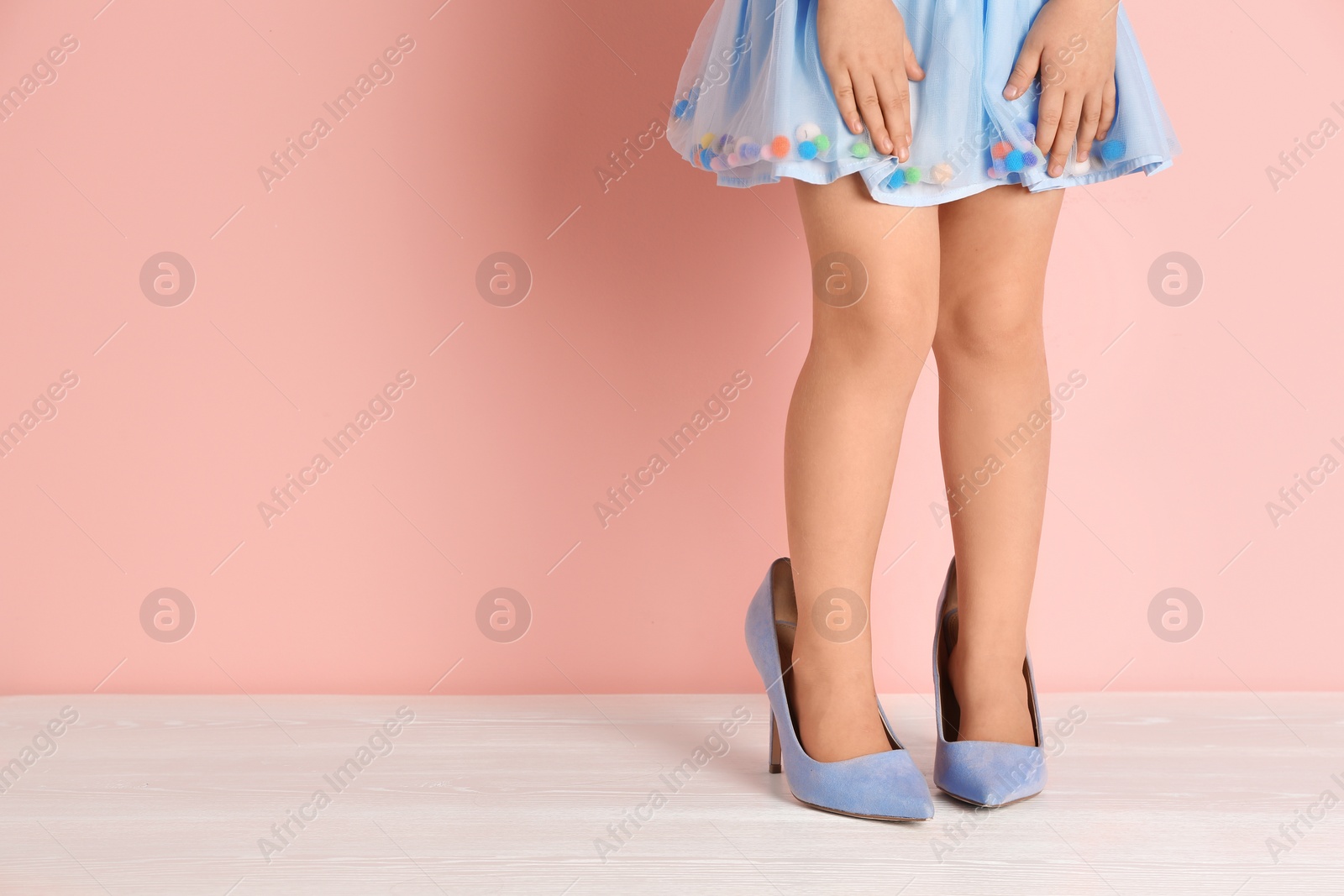 Photo of Little girl in oversized shoes near color wall with space for text, closeup on legs