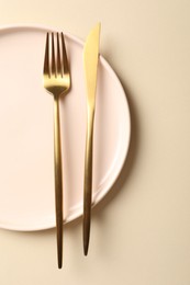 Photo of Stylish golden cutlery and plate on beige background, top view