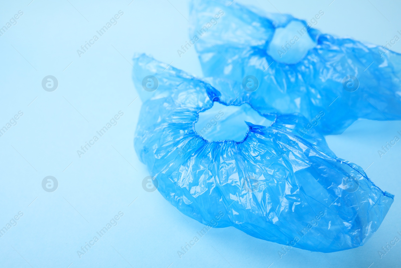 Photo of Pair of medical shoe covers on light blue background, space for text