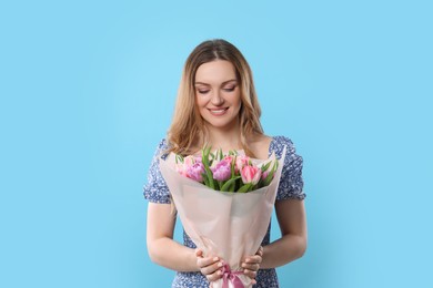 Happy young woman with bouquet of beautiful tulips on light blue background