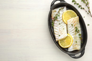 Photo of Fresh raw cod fillets with thyme and lemon in baking dish on white wooden table, top view. Space for text