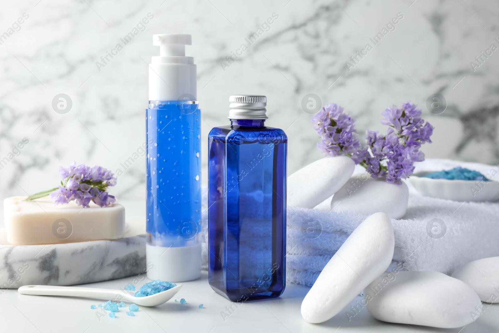 Photo of Spa composition. Bottles of cosmetic products, sea salt, stones, soap and flowers on white table