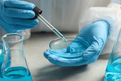 Photo of Scientist dripping liquid from pipette into petri dish at table, closeup