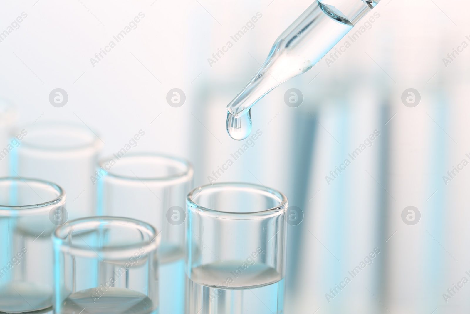 Photo of Laboratory analysis. Dripping liquid from pipette into glass test tube on blurred background, closeup