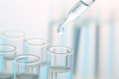 Laboratory analysis. Dripping liquid from pipette into glass test tube on blurred background, closeup