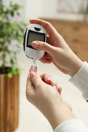 Diabetes. Woman checking blood sugar level with glucometer at home, closeup