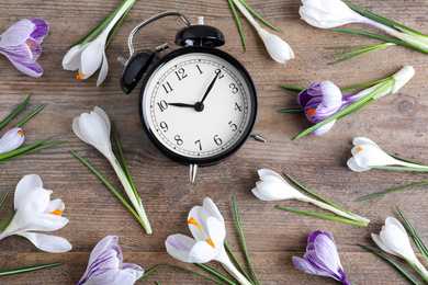 Black alarm clock and spring flowers on wooden table, flat lay. Time change
