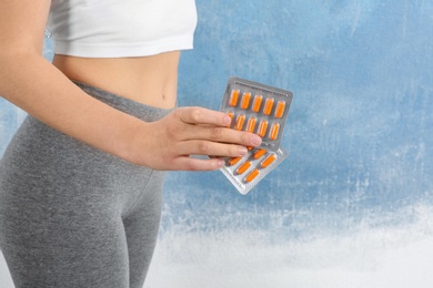 Photo of Slim woman holding weight loss pills in blister packs against color background, closeup. Space for text