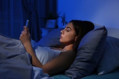 Photo of Young woman with mobile phone at night. Bedtime