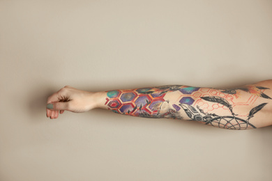 Woman with colorful tattoos on arm against beige background, closeup