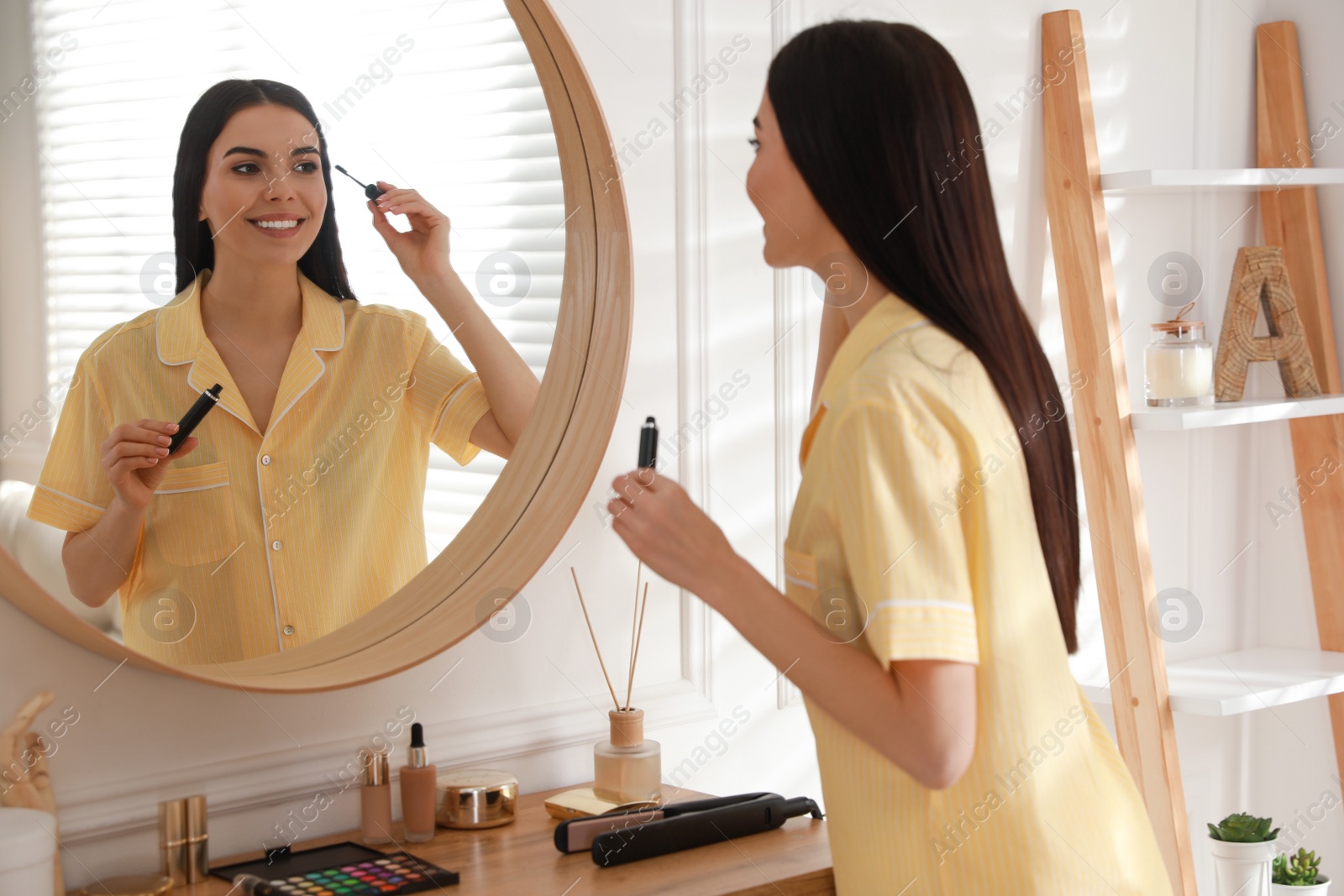 Photo of Young woman doing makeup near mirror at home. Morning routine
