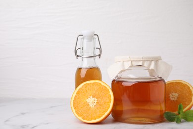 Photo of Tasty kombucha, orange and mint on white marble table, space for text