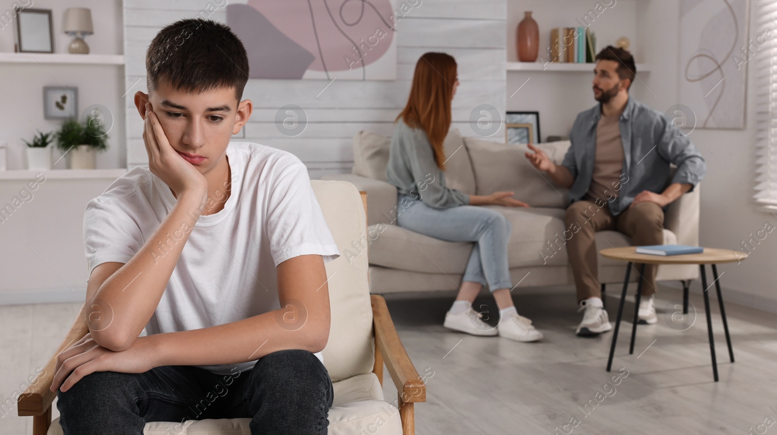 Photo of Unhappy teenage boy sitting in armchair while his parents arguing on background. Problems at home