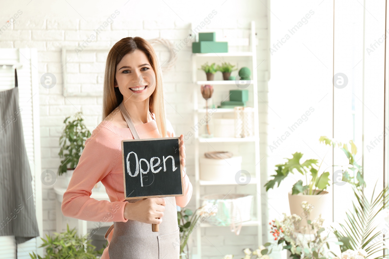 Photo of Female florist holding OPEN sign at workplace