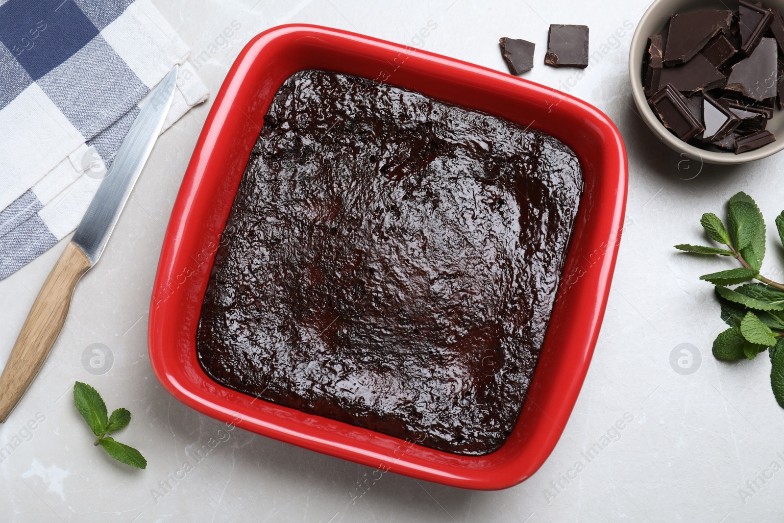 Photo of Delicious brownie in baking dish, pieces of chocolate and fresh mint on light grey table, flat lay