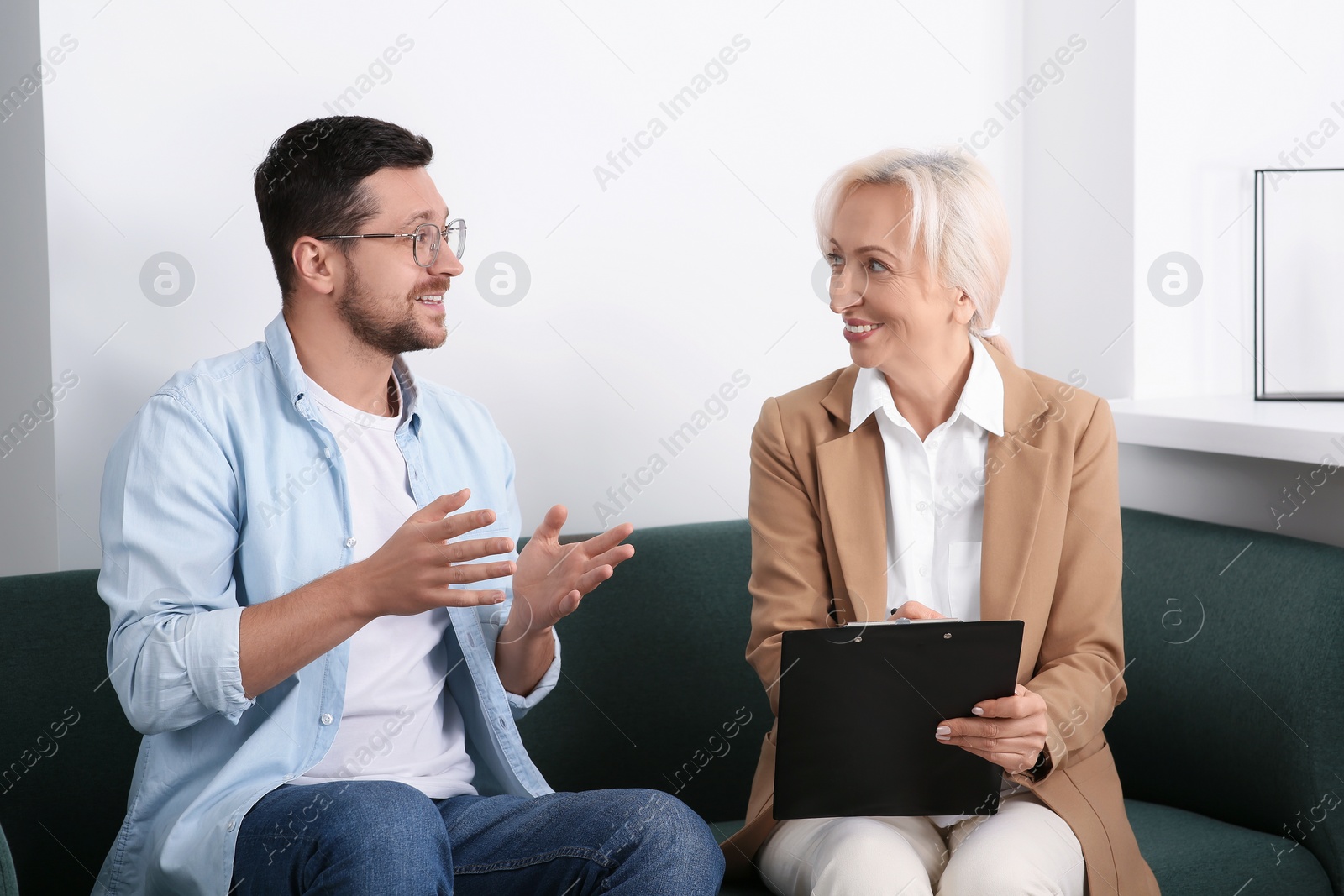 Photo of Happy woman having conversation with man on sofa in office. Manager conducting job interview with applicant