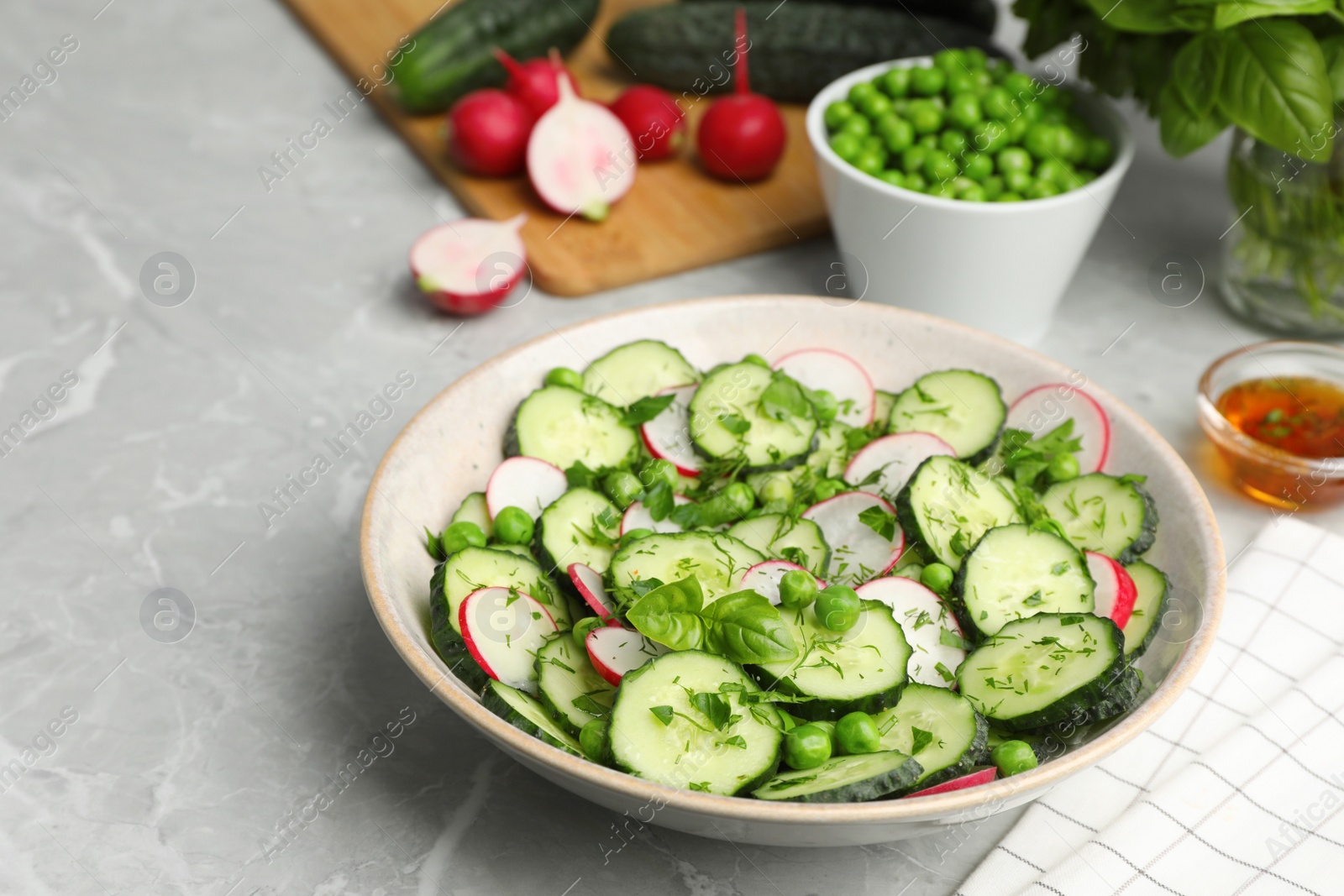 Photo of Appetizing salad with cucumbers, radish and pea in bowl on light grey table