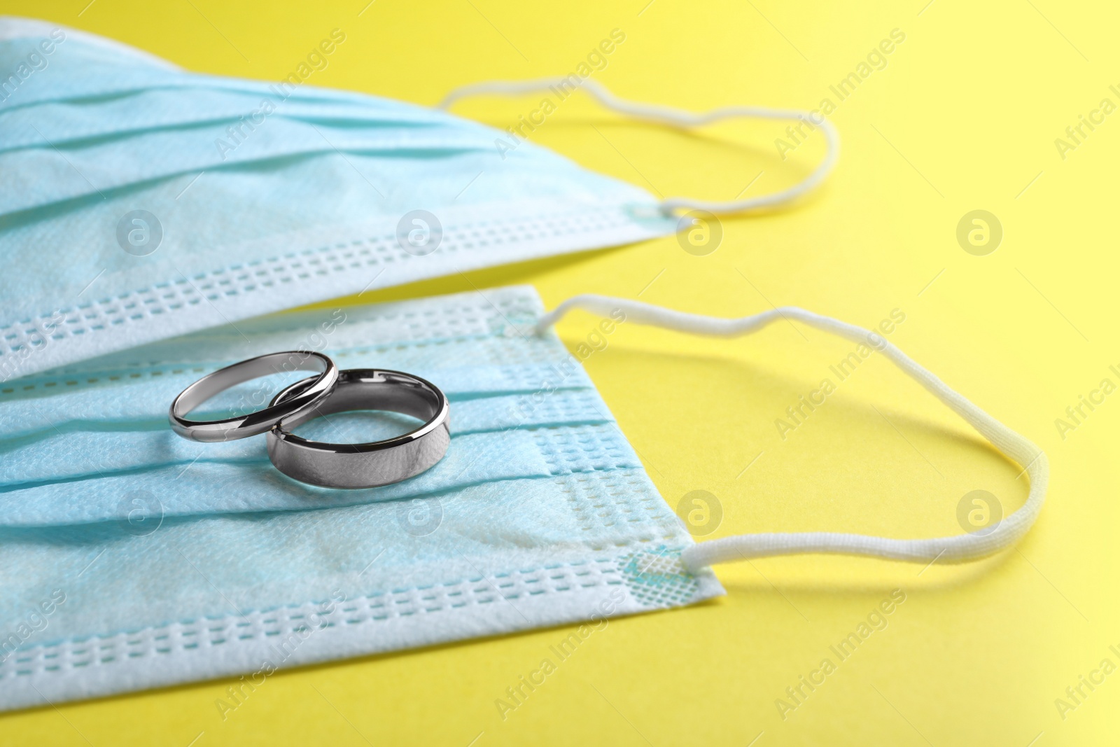 Photo of Protective masks and wedding rings on yellow background. Divorce during coronavirus quarantine