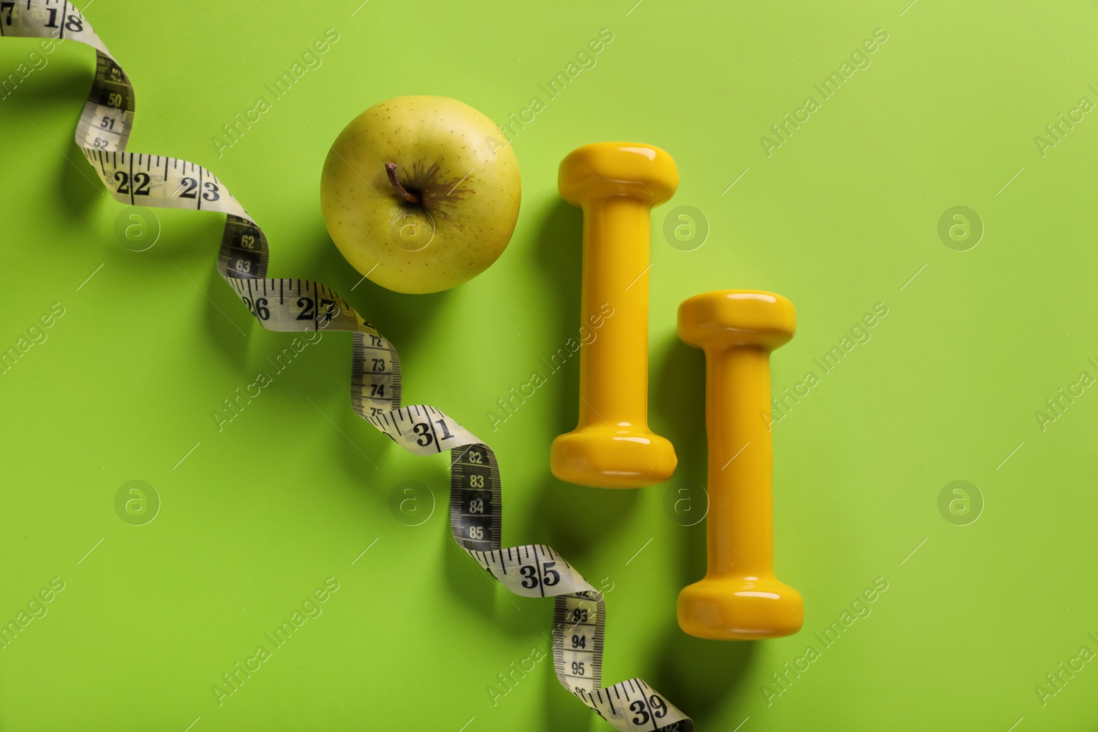 Photo of Measuring tape, dumbbells and apple on light green background, flat lay. Weight control concept