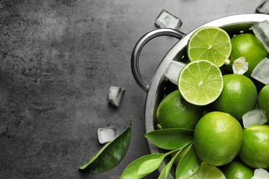 Photo of Colander with fresh ripe limes and ice cubes on gray background, top view