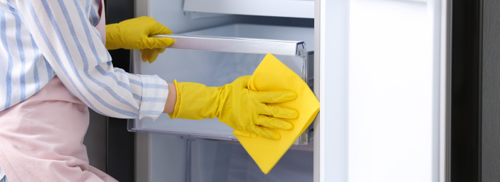 Woman in rubber gloves cleaning refrigerator, closeup. Banner design