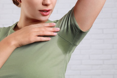 Photo of Young woman with sweat stain on her clothes against brick wall, closeup. Using deodorant