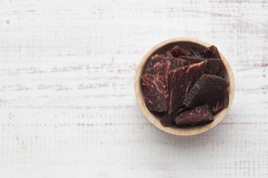 Photo of Delicious beef jerky in bowl on wooden table, top view. Space for text